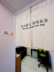 A fabric curtain with text in Chinese, partially covering an entrance. The text includes phrases in both Chinese and English, suggesting themes of listening and environment. The background shows a glimpse of an office space.