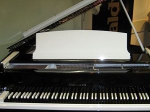 Close-up view of a glossy black grand piano with open lid, featuring white keys and a blank music rest.