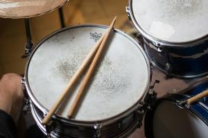 Top view of a snare drum with two wooden drumsticks resting on the drumhead.