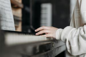 A close-up of a person's hand playing piano keys, with sheet music visible in the background.