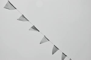 Black and white image of triangular bunting flags hanging against a light gray sky.