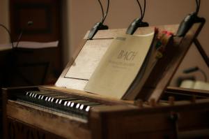 A close-up view of a wooden harpsichord with sheet music titled 'Bach' displayed on top.
