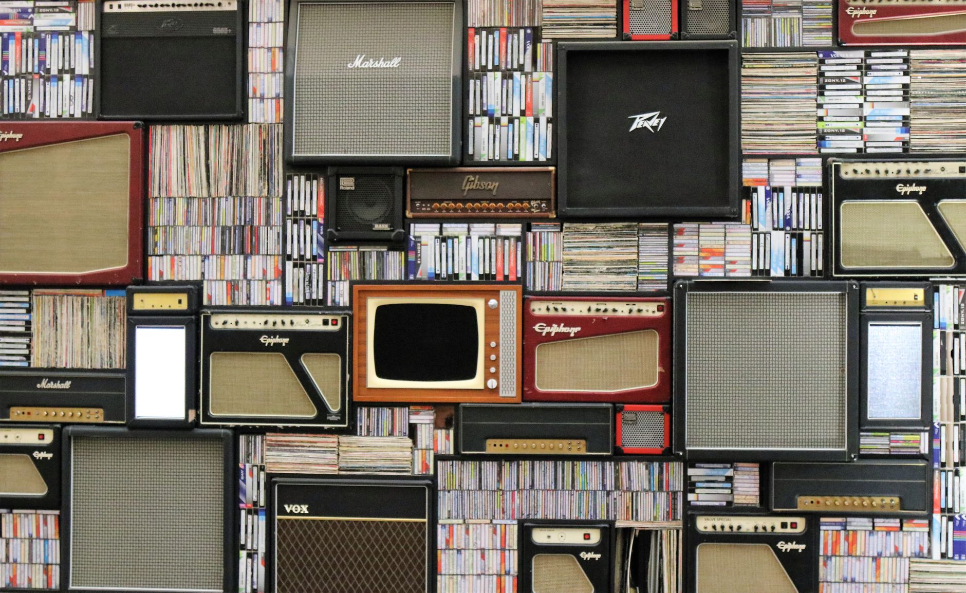 Wall covered with vintage guitar amplifiers and stacks of cassette tapes